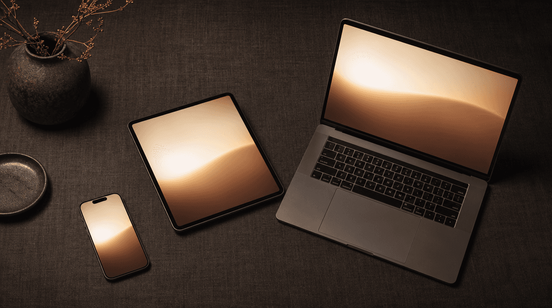 Wide editorial flat-lay. Multiple device forms — a smartphone, a compact tablet, and a small laptop — arranged on a dark