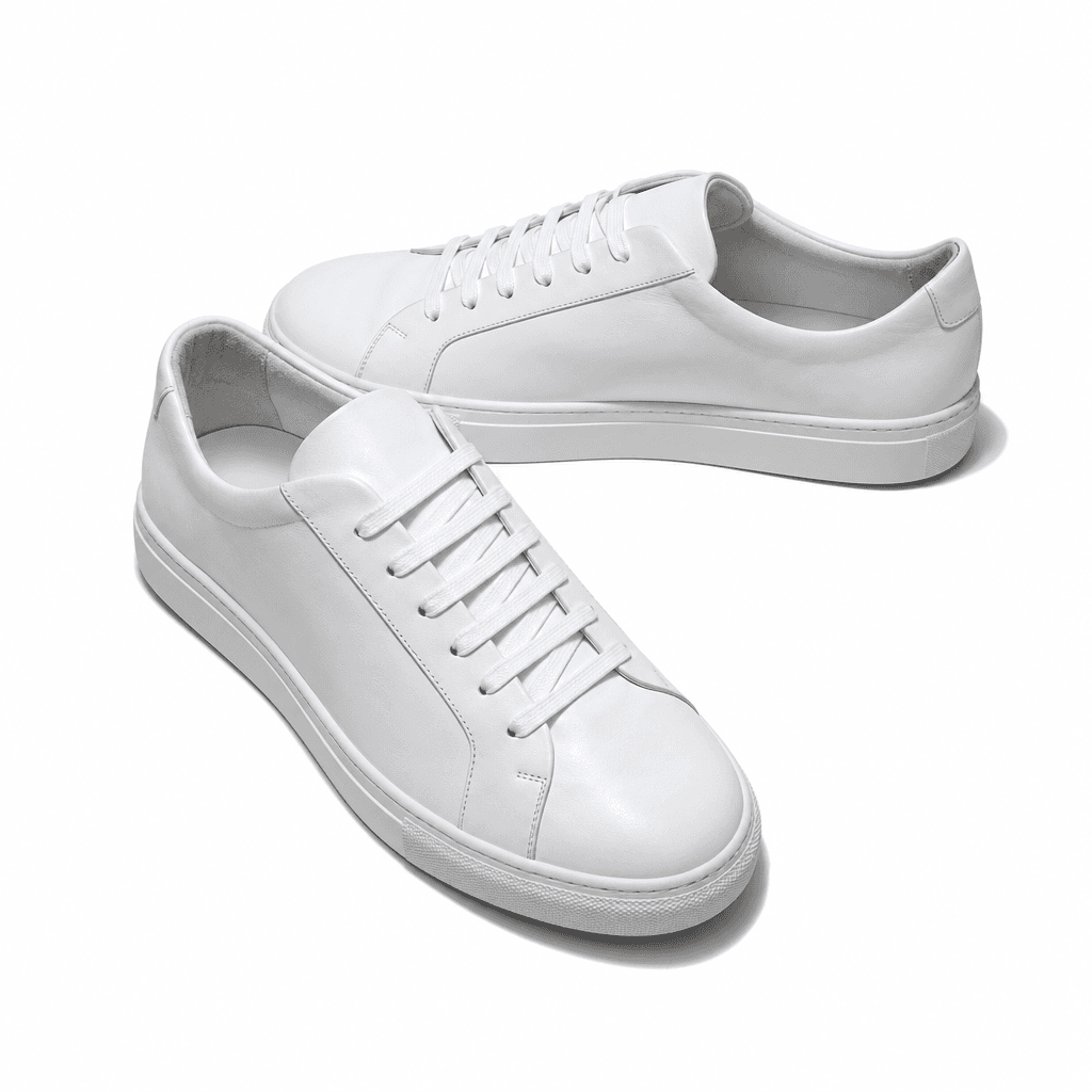A pair of minimalist white leather sneakers shot on a seamless pure white studio surface, overhead editorial lighting, s