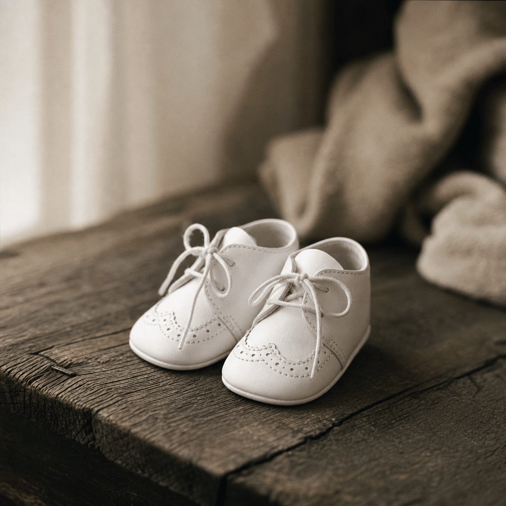 Editorial macro shot of a tiny pair of white baby shoes resting on weathered dark oak, soft diffused window light from t
