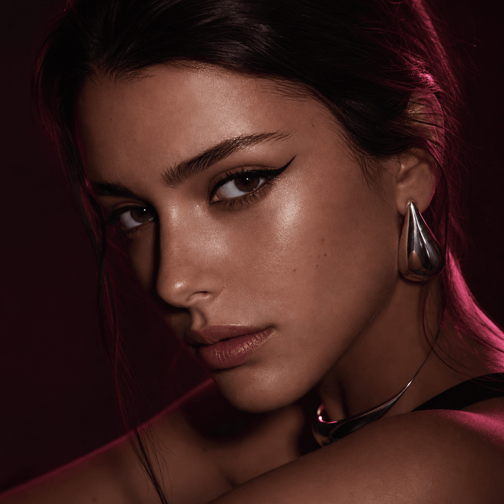 A fictional beauty campaign character with graphic eyeliner and understated metallic accessories, close portrait framed