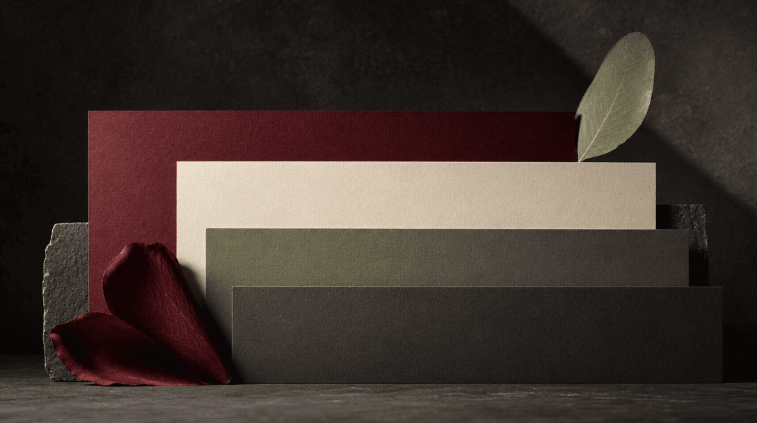 An abstract still life of stacked matte color cards derived from deep red petals, pale cream paper, sage leaves, and cha