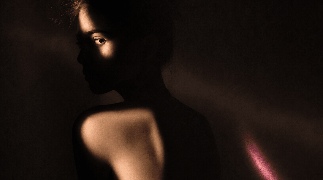 An abstract human silhouette formed by warm portrait light against a deep charcoal backdrop, soft skin-toned reflections