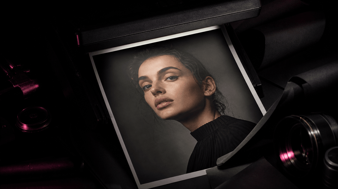 A finished portrait print emerging from darkness beneath a focused studio beam, surrounded by matte black material, a vi