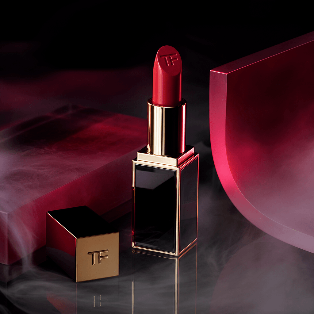 A glossy lipstick tube resting on a smoked mirror with soft haze drifting across the foreground, deep black backdrop, fo