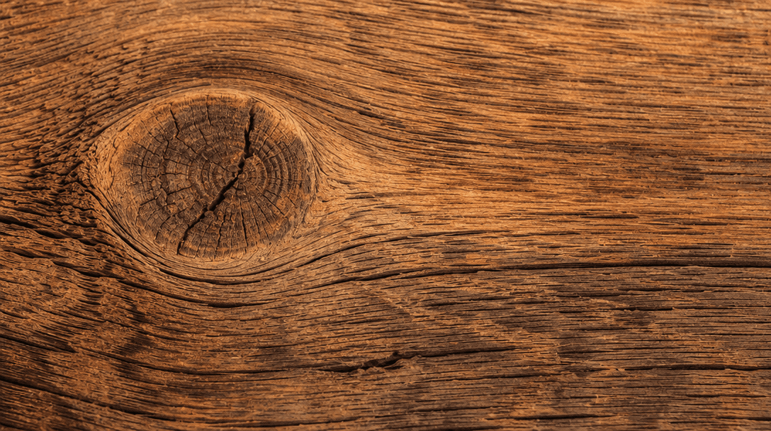 Extreme close-up of rustic wood grain texture with warm studio lighting. Visible knots, weathering, and natural grain pa