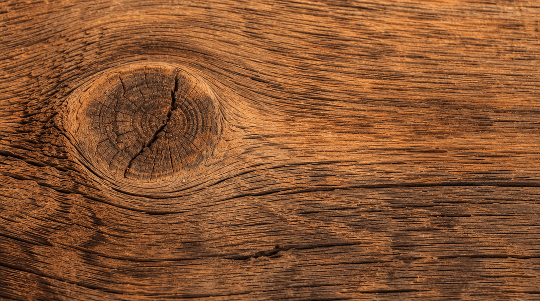 Extreme close-up of rustic wood grain texture with warm studio lighting. Visible knots, weathering, and natural grain pa