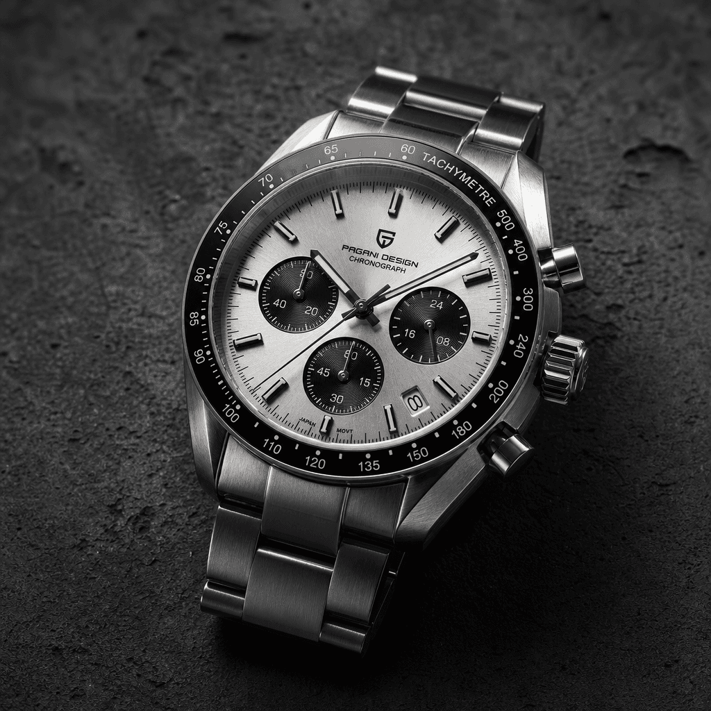 Square editorial product shot: a sleek silver chronograph watch placed on dark textured concrete. Side-lit to emphasise