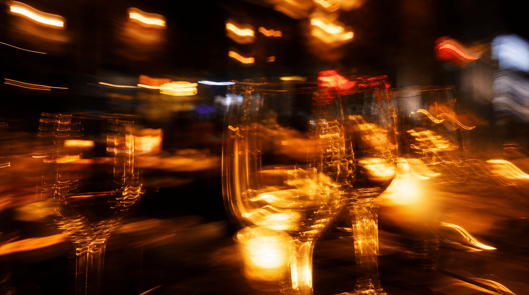 Abstract motion blur of warm bokeh lights in a vibrant evening restaurant scene — out-of-focus candles, wine glasses, an