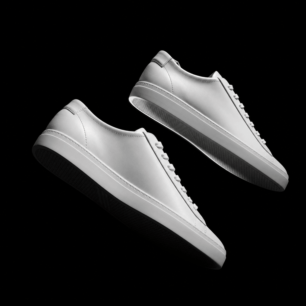 High-fashion footwear editorial: a pair of minimalist white leather sneakers floating at a slight angle against a pure b