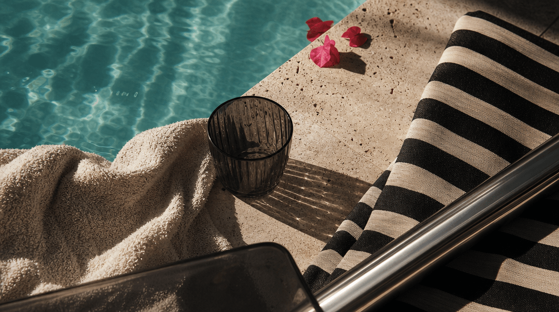 A sequence of poolside materials arranged as an editorial landscape: turquoise water, cream terry cloth, smoked glass, s