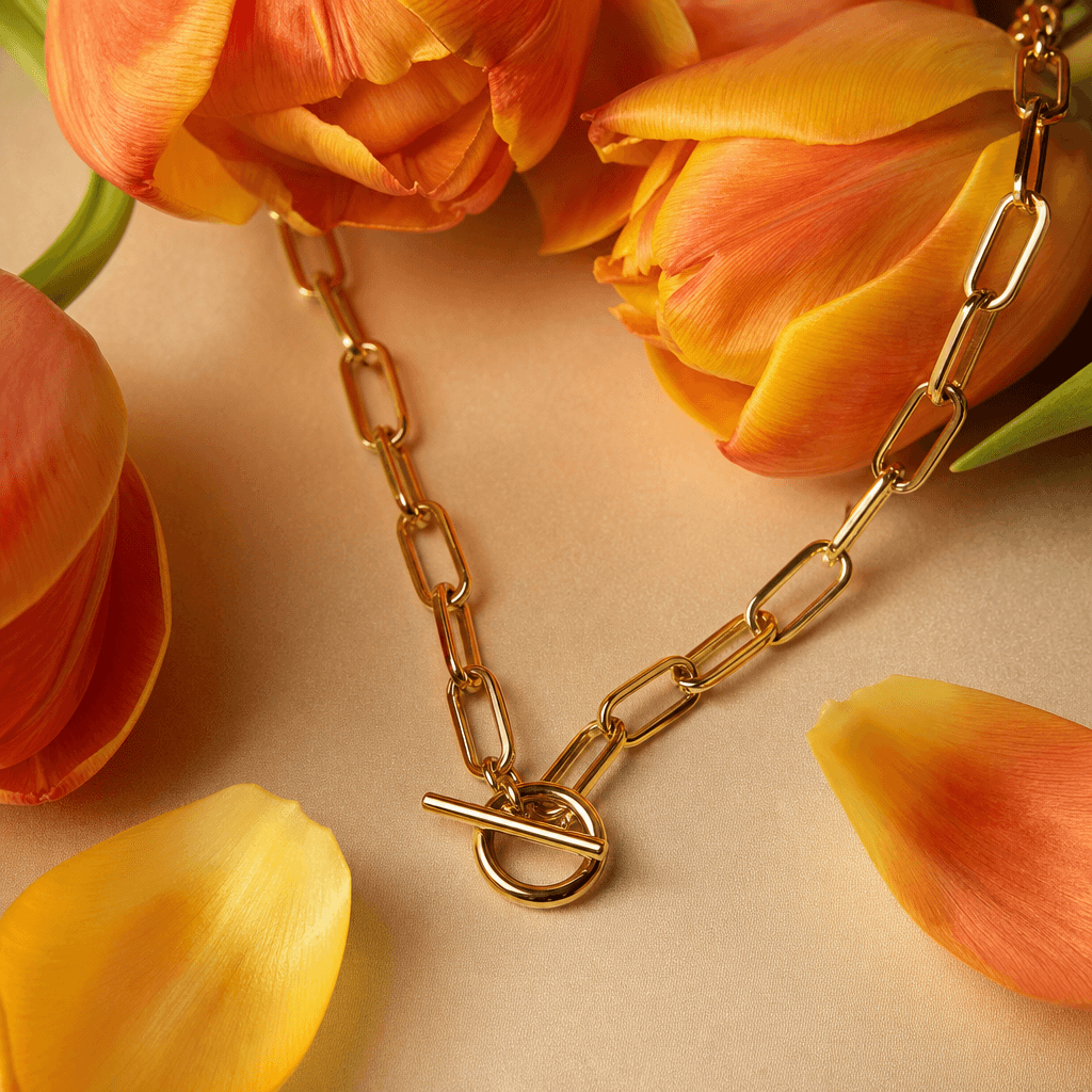 Gold chain necklace with warm-colored tulip petals arranged artfully around it in botanical styling, close-up macro lens