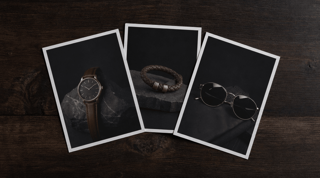Minimalist editorial arrangement of three small product prints on matte paper fanned slightly on a dark wooden surface,