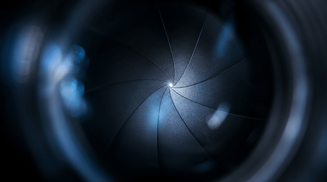 Abstract macro photograph of camera lens aperture blades open to a single sharp focal point, radiating soft bokeh haze o