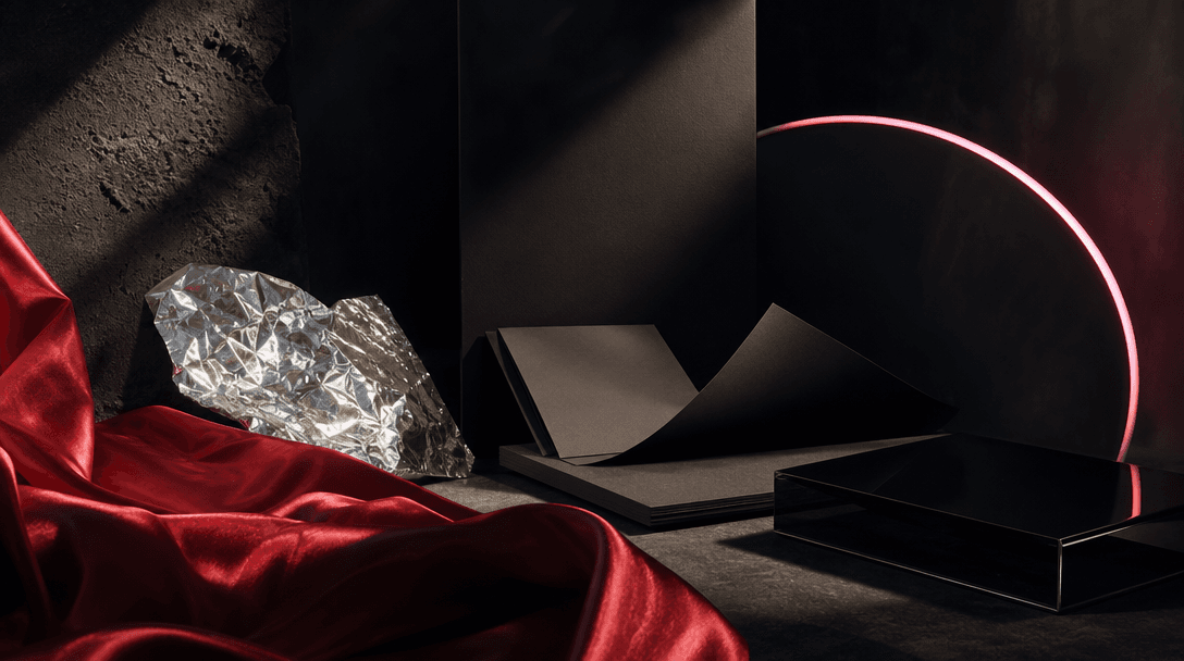 Several distinct cinematic materials arranged in a dark creative studio: red satin, matte paper, glossy black acrylic, s