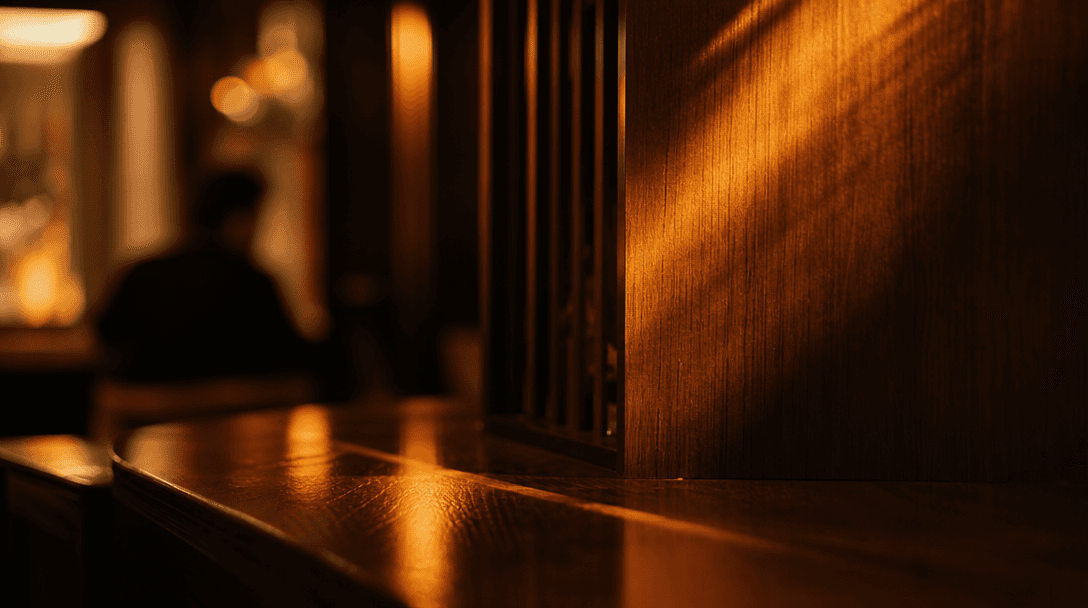 Abstract close-up of warm amber light rays falling across dark polished wood surfaces in a restaurant interior, soft dep