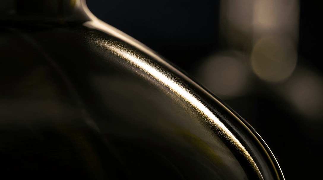Extreme macro of a dark glass bottle surface catching dramatic sidelight: razor-sharp specular highlight streak, shallow