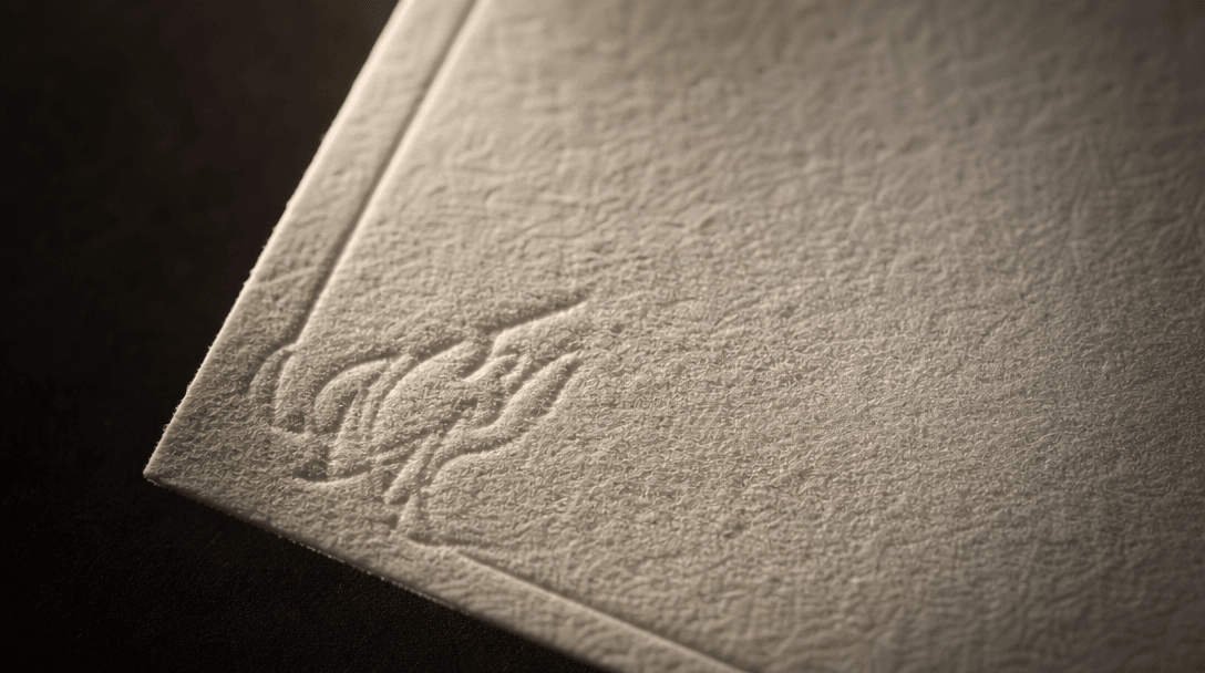 Extreme macro texture study of premium cream cotton paper with a subtly embossed press pattern, raking warm directional